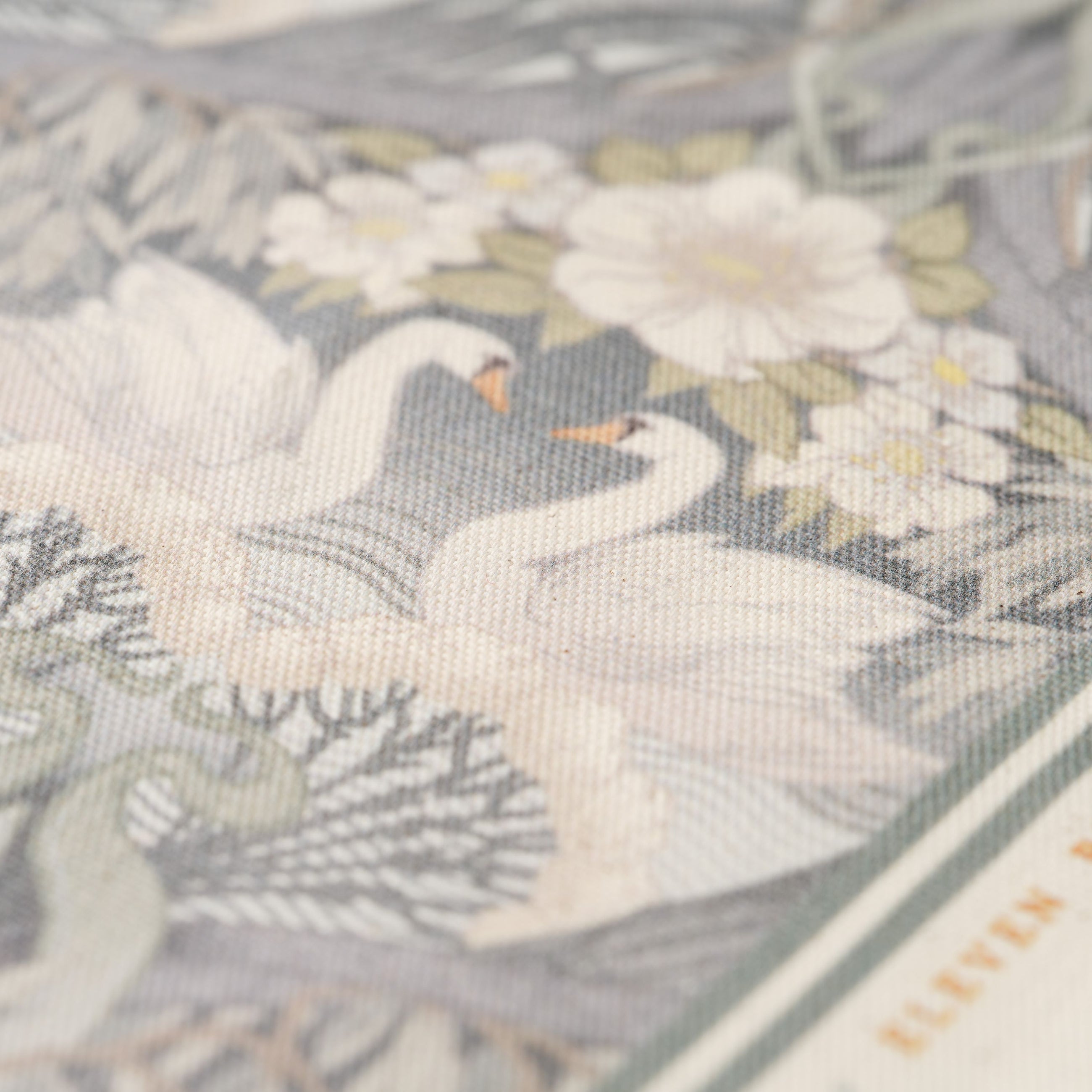 Close up of Bibury Swan tea towel with swan and floral pattern on a grey background