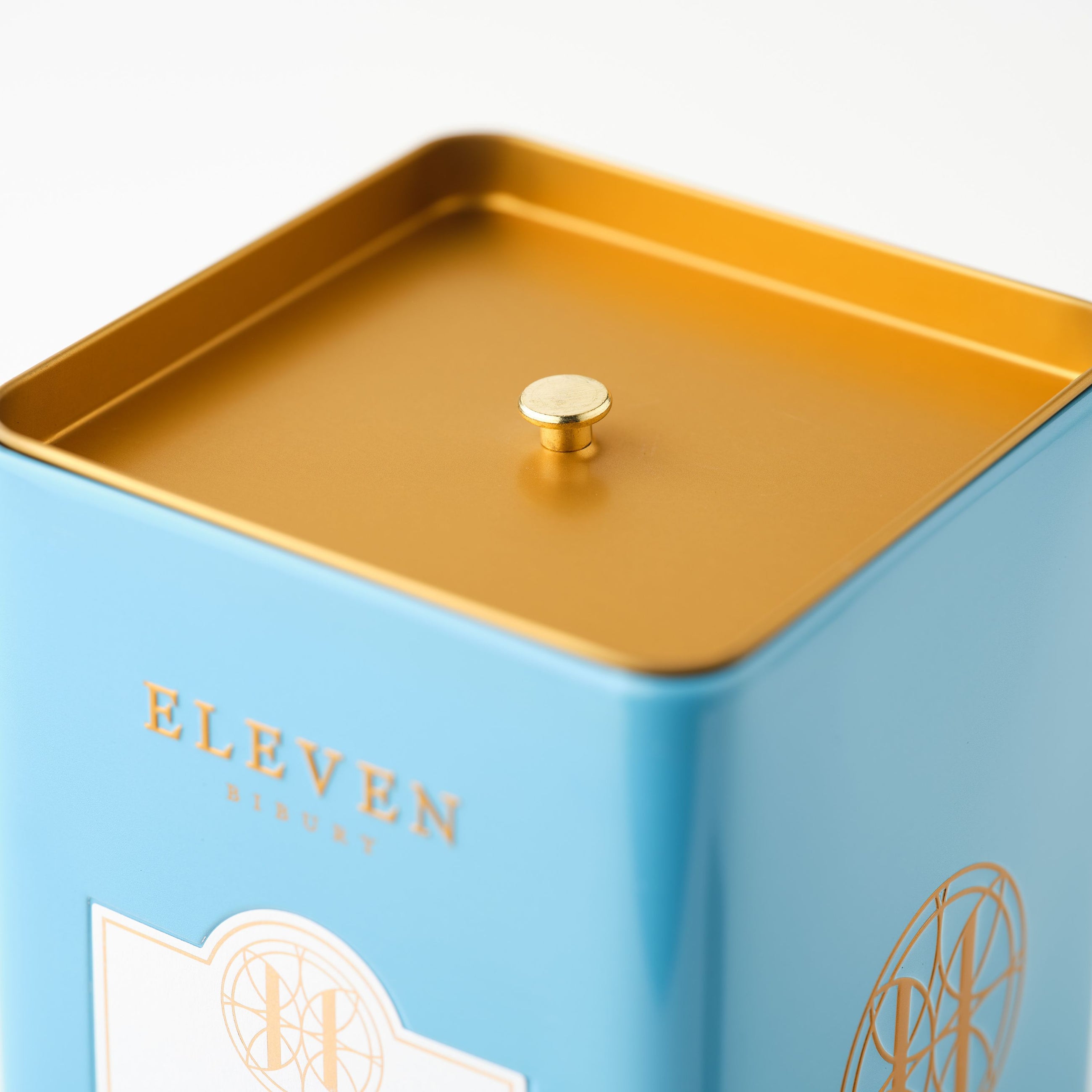 Blue metal tin with gold lid and 'ELEVEN Bibury' branding on a white background