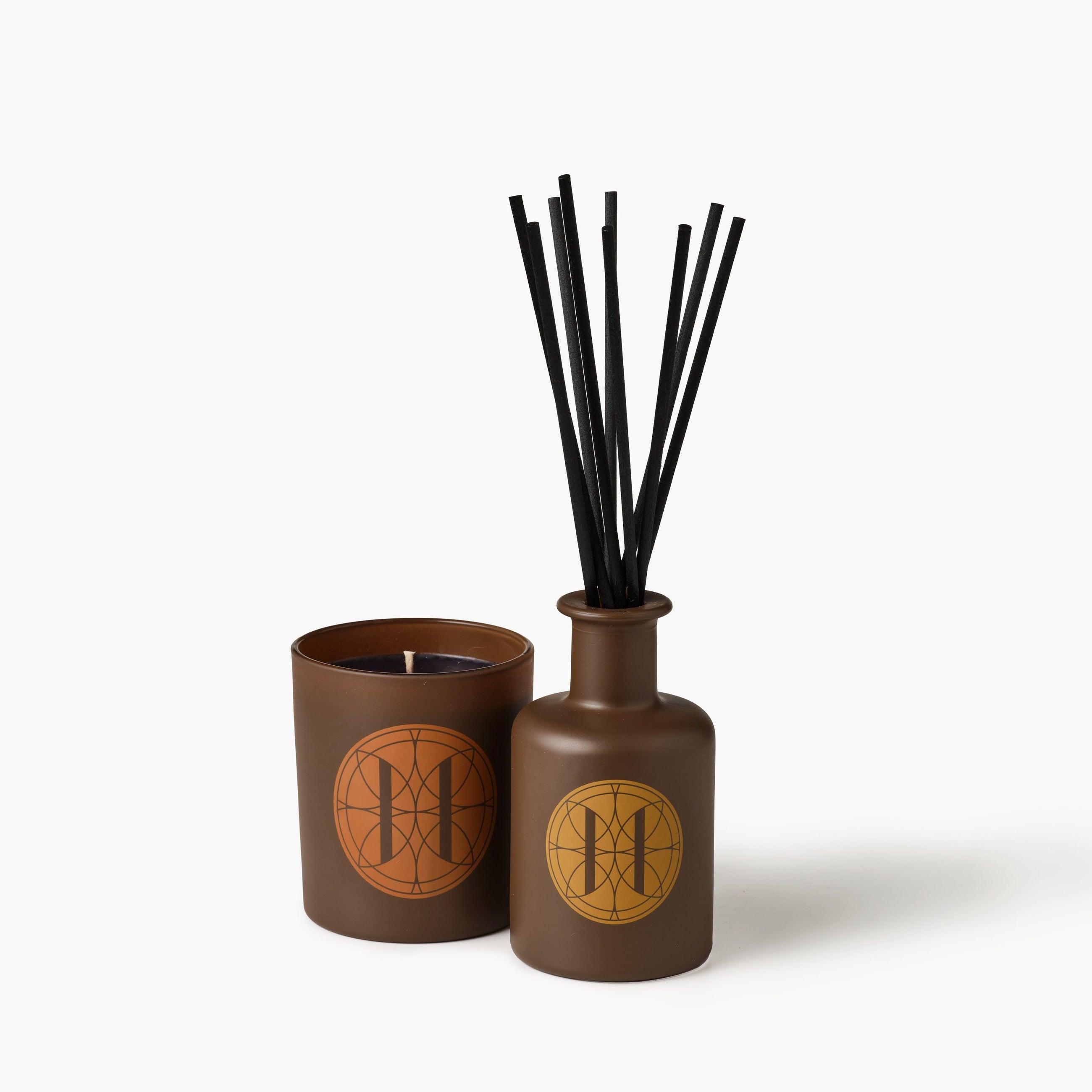 Eleven Bibury 'Gabriel's Muse' brown diffuser bottle with black sticks and matching candle on a white background