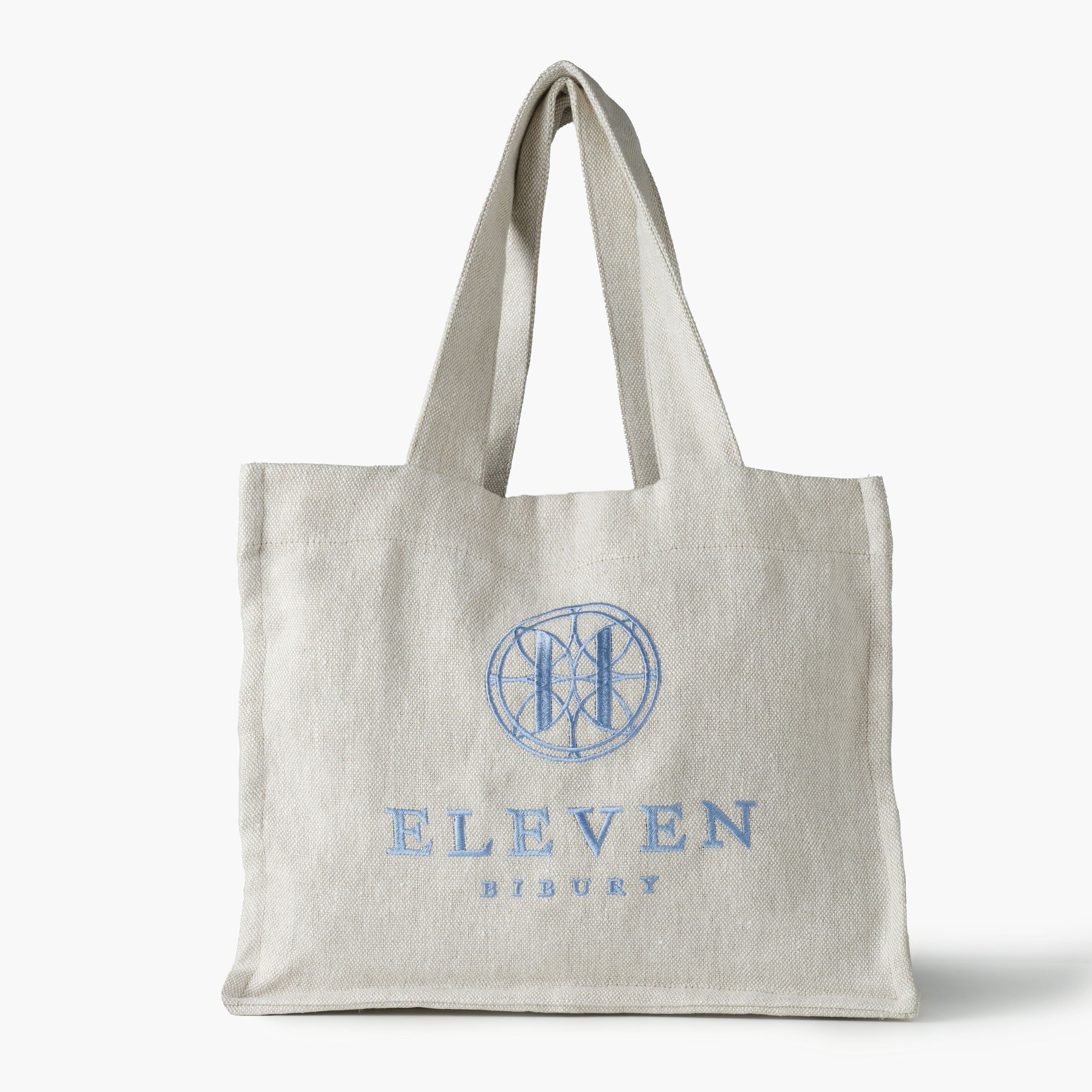 Natural linen tote bag with embroidered blue Eleven Bibury logo on a white background