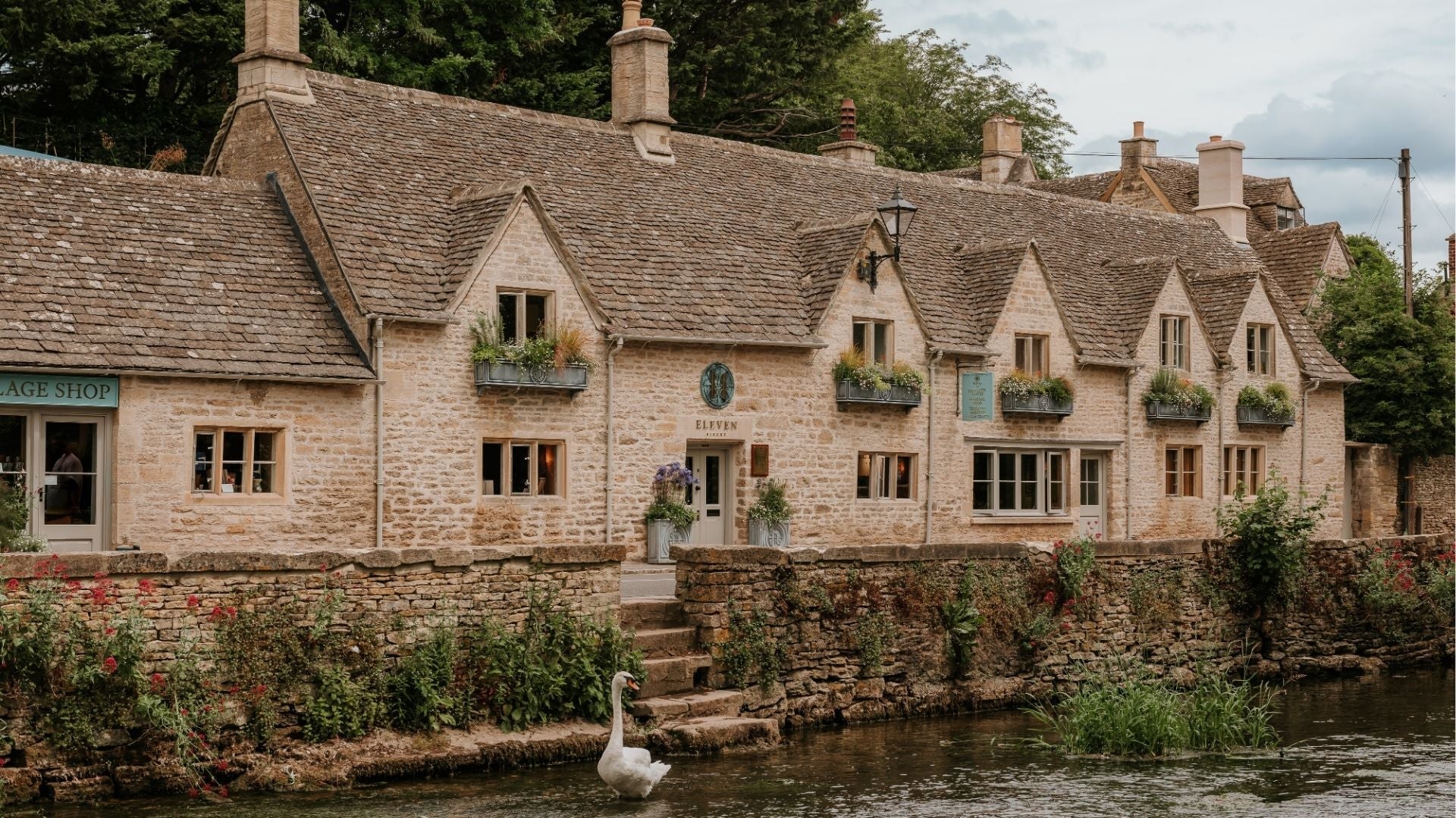 A photo of the front of Eleven Bibury with a swan on the River Coln