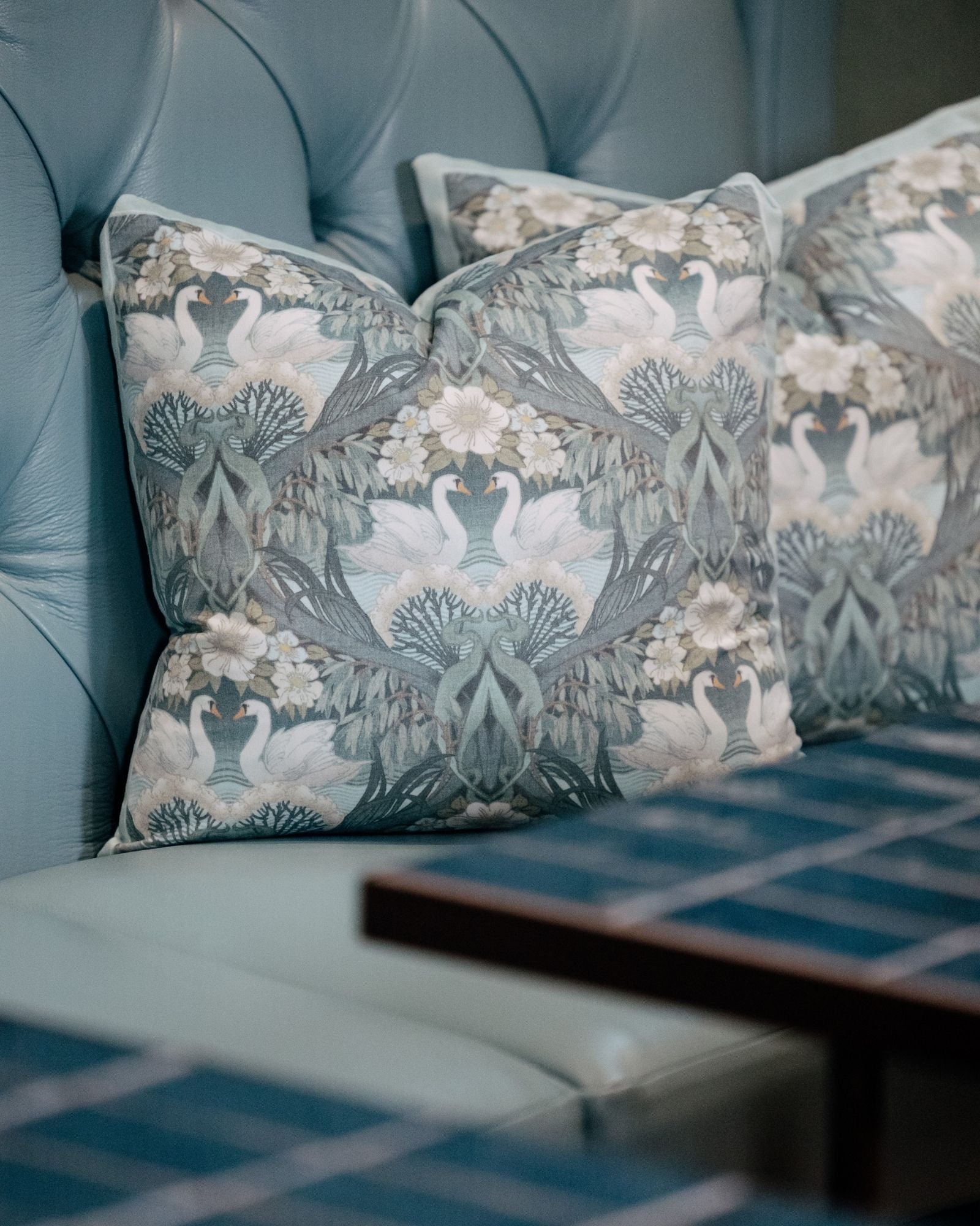 Decorative pillows with floral and bird pattern on a blue upholstered chair.