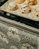 Baked scones on a baking tray with a floral-patterned tea towel handing on oven door in the foreground.