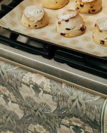 Baked scones on a baking tray with a floral-patterned tea towel handing on oven door in the foreground.