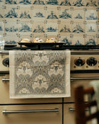 Stove with a decorative towel hanging on the handle against a patterned wall.