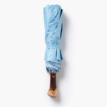 Folded light blue umbrella with a wooden handle on a white background