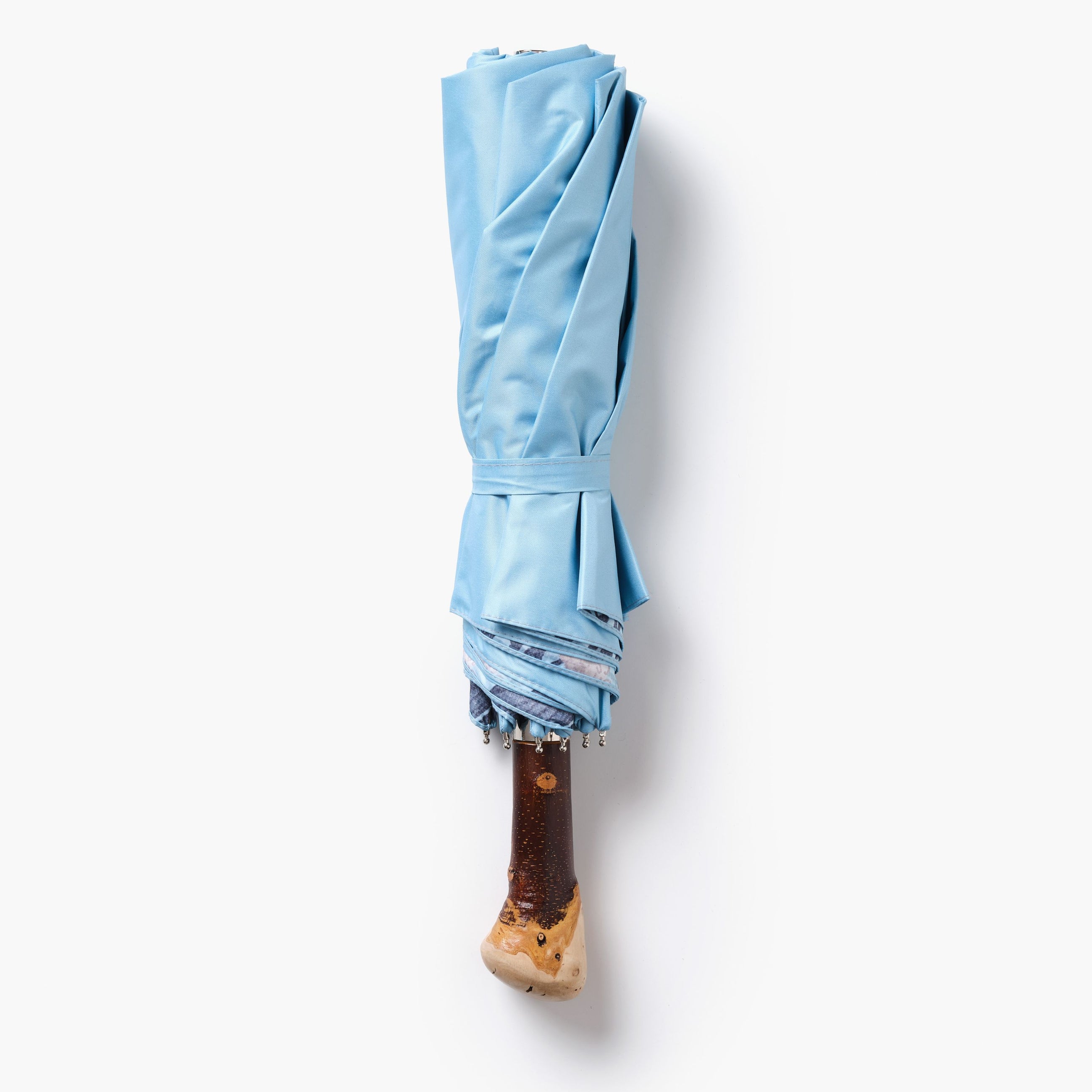 Folded light blue umbrella with a wooden handle on a white background