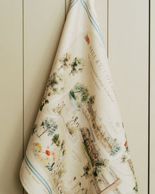 Decorative towel with vintage-style map and illustration design against a painted wooden background