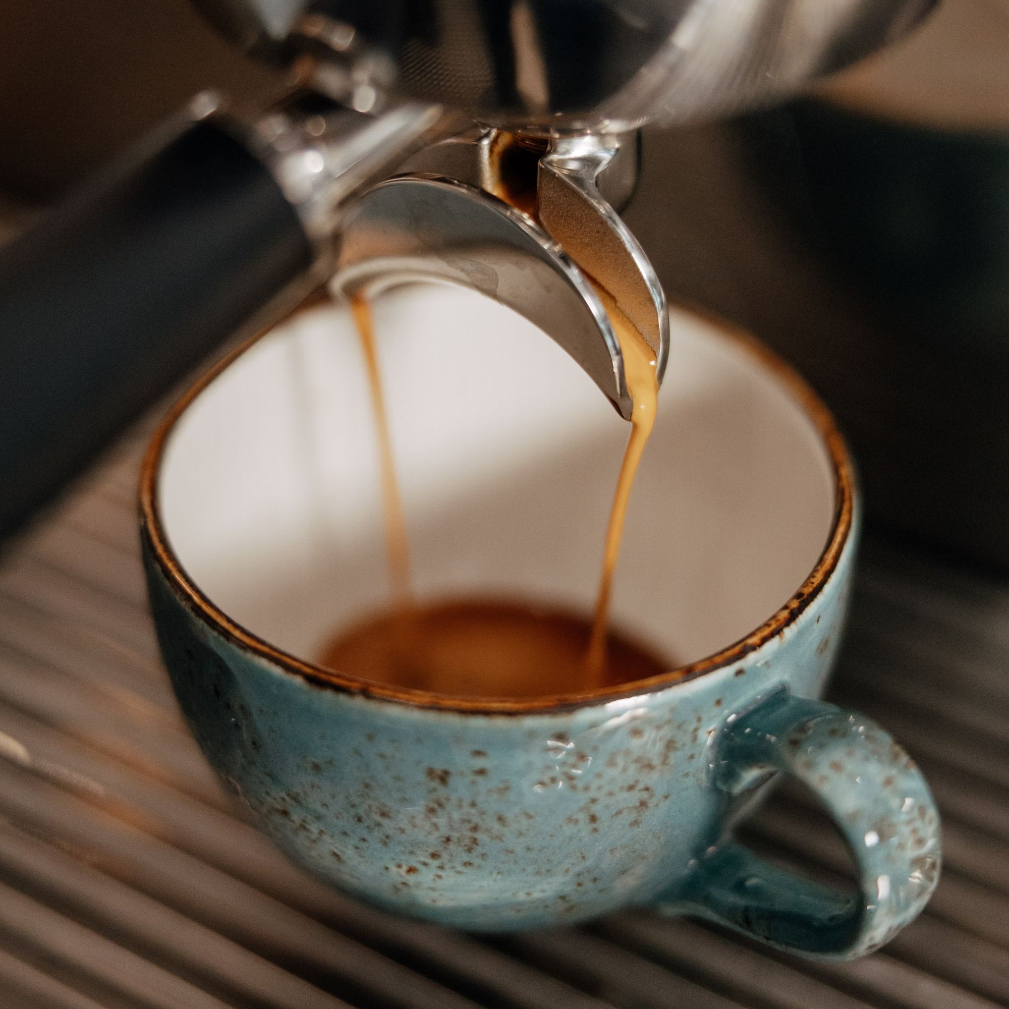 Espresso being poured into a blue ceramic cup from a coffee machine.