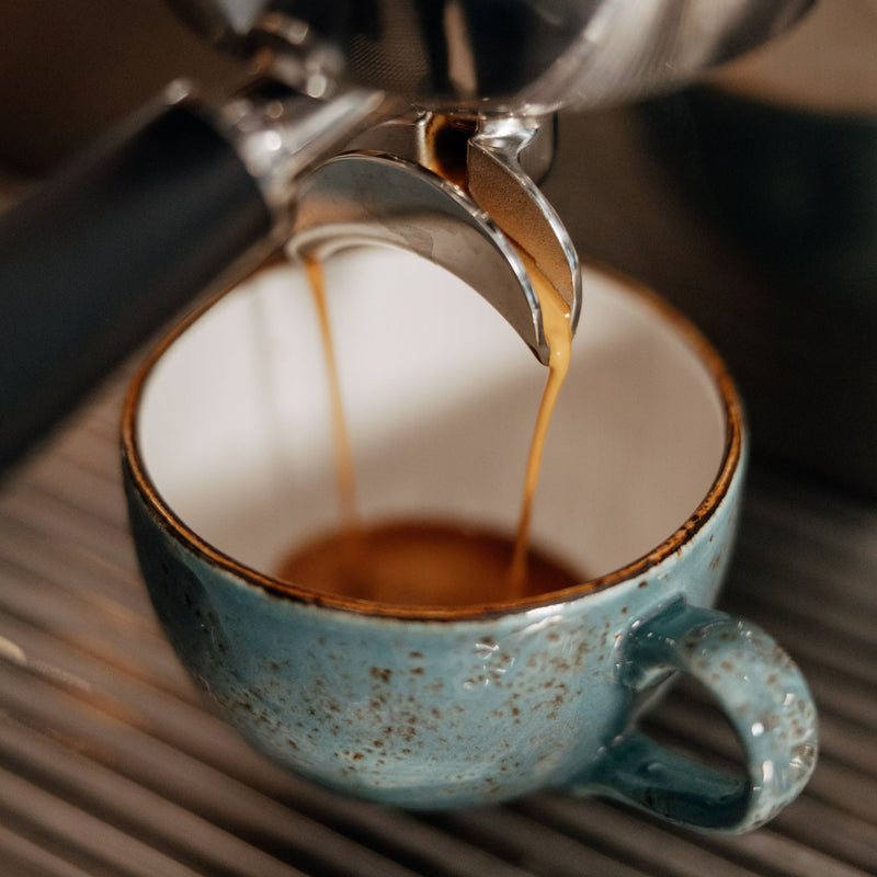 Espresso being poured into a blue ceramic cup from a coffee machine.