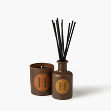 Eleven Bibury 'Gabriel's Muse' brown diffuser bottle with black sticks and matching candle on a white background