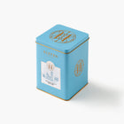 Blue tea canister with gold accents and a Eleven Bibury Hot Chocolate label on a white background