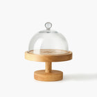 Round wooden cake stand engraved with Eleven Bibury logo with a glass dome on a white background