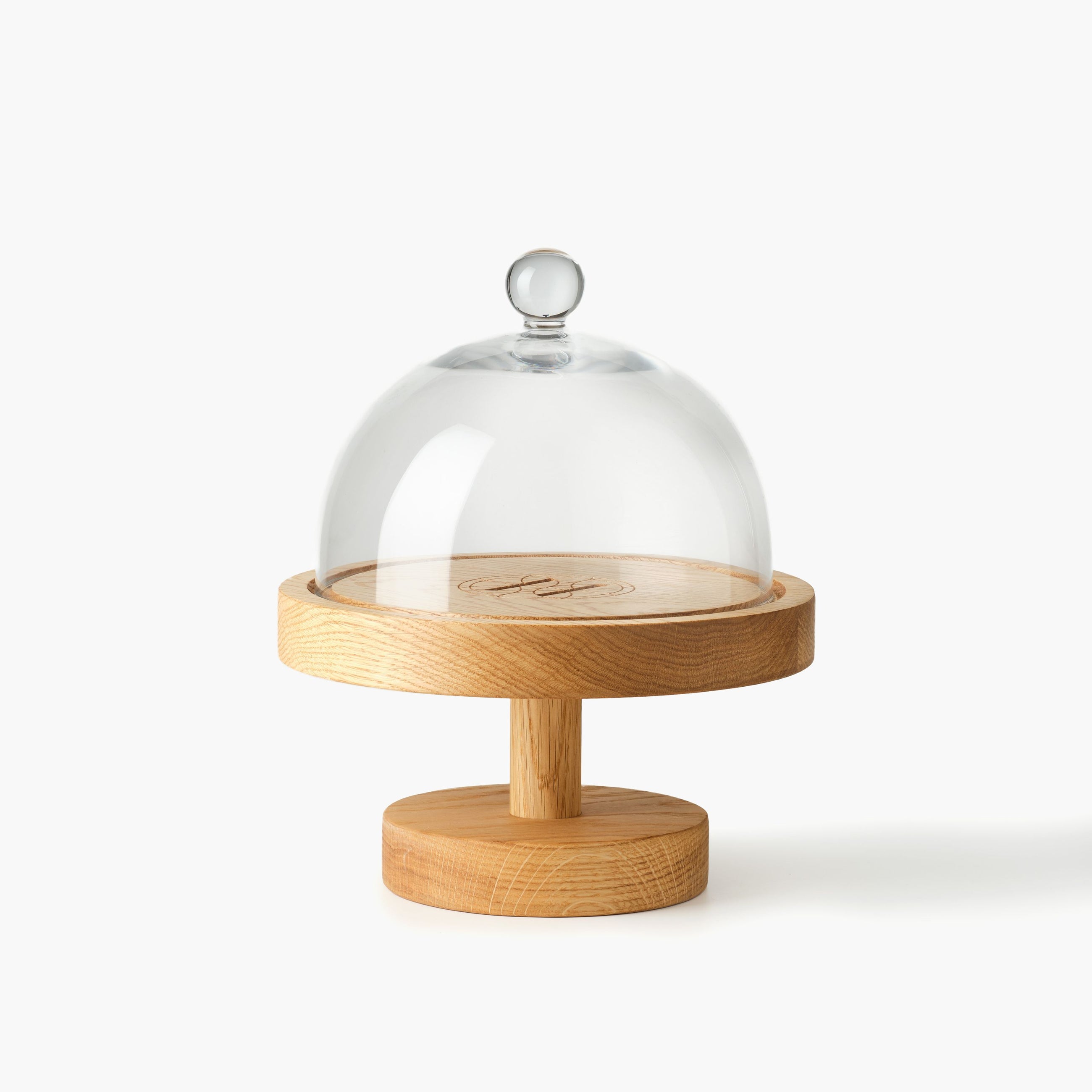 Round wooden cake stand engraved with Eleven Bibury logo with a glass dome on a white background
