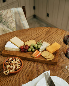 Wooden cheeseboard with assorted cheeses, fruits, and nuts on a wooden table.