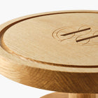 Close up of round wooden pedestal cake stand with engraved Eleven Bibury logo on a white background