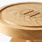 Round wooden pedestal cake stand with Eleven Bibury engraved logo on a white background