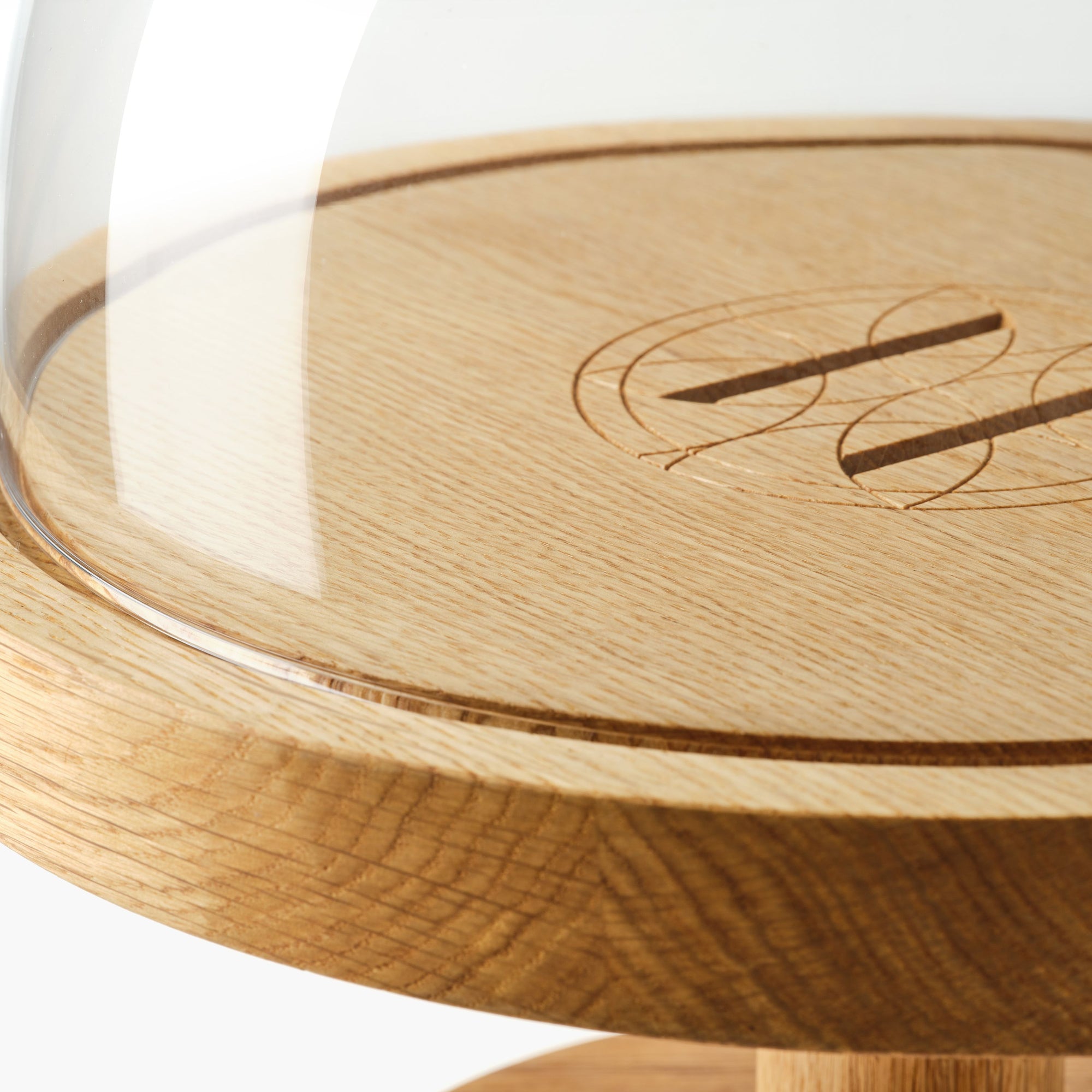 Close-up of oak pedestal cake stand with glass dome and Eleven Bibury engraved logo on a white background.