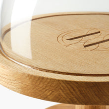Close-up of oak pedestal cake stand with glass dome and Eleven Bibury engraved logo on a white background.