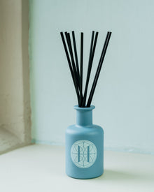 Blue diffuser bottle with black sticks on windowsill