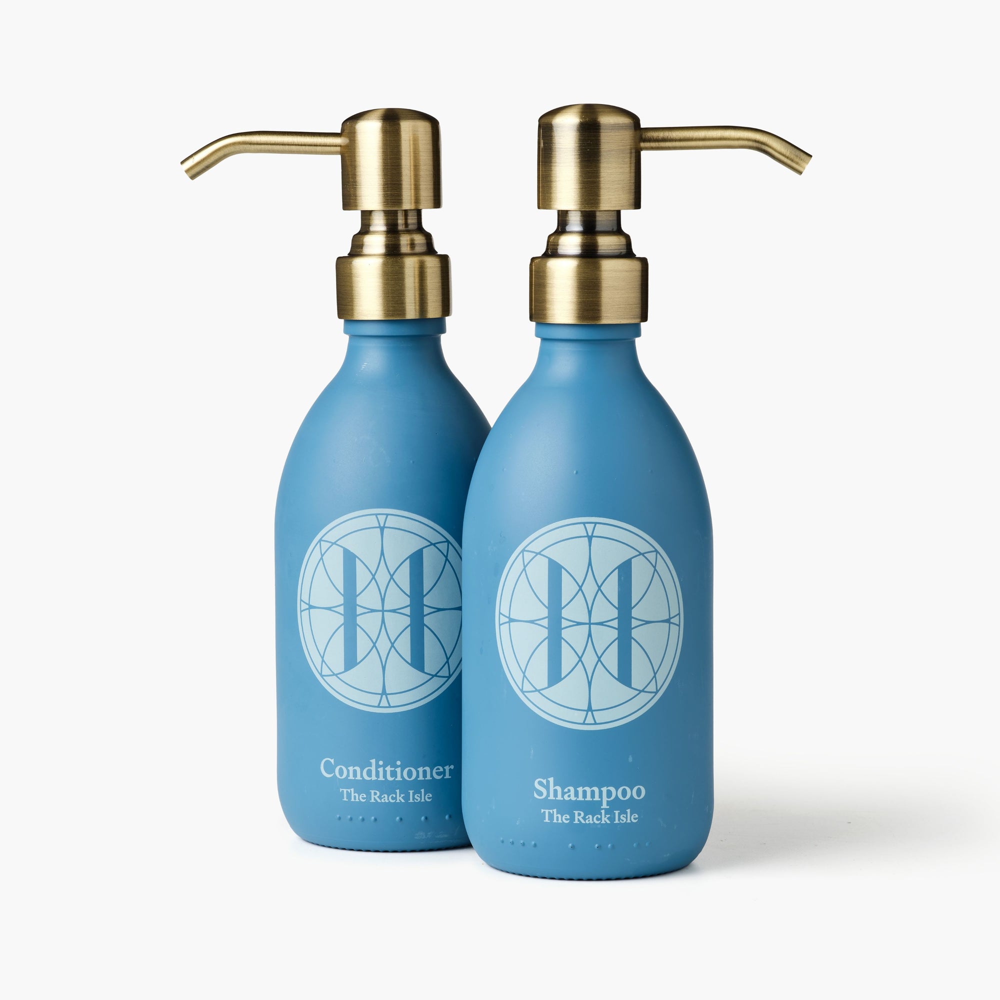 Eleven Bibury 'Rack Isle' blue shampoo and conditioner bottles with gold pumps on a white background