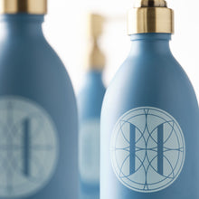 Close up of Eleven Bibury 'Rack Isle' blue bottles with gold caps and a logo on a blurred background