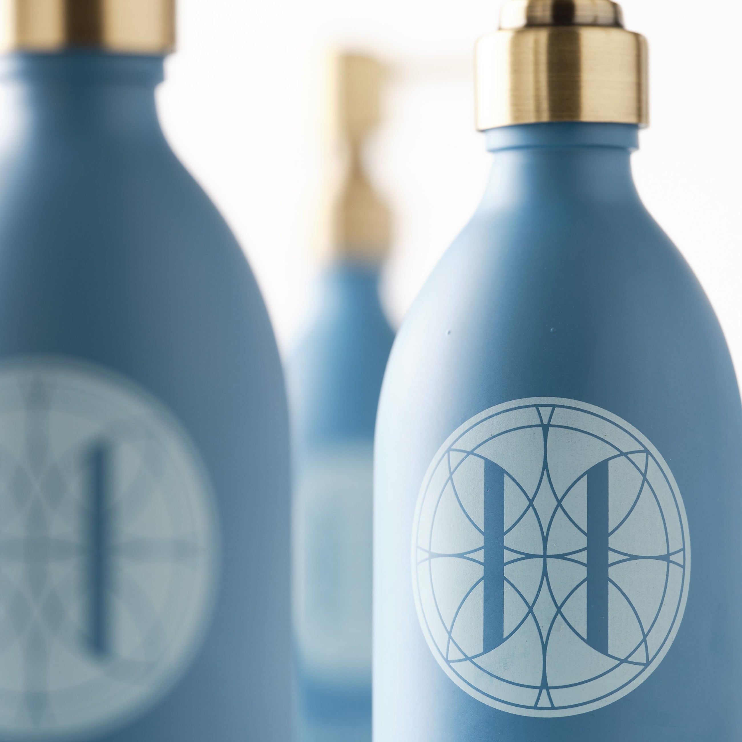 Close up of Eleven Bibury 'Rack Isle' blue bottles with gold caps and a logo on a blurred background