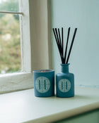 Rack Isle candle and diffuser with black sticks on a windowsill.