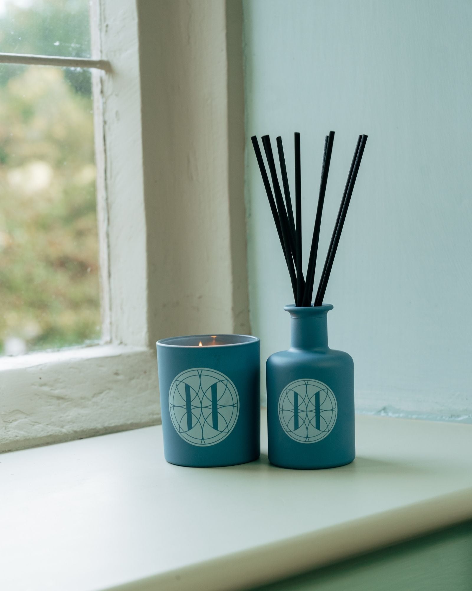 Rack Isle candle and diffuser with black sticks on a windowsill.
