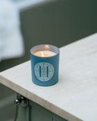 Blue candle in a glass jar with Eleven Bibury logo on a bathroom counter