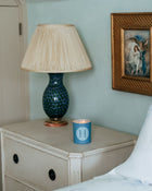 Nighstand with blue lamp and Rack Isle candle, framed artwork on wall