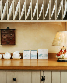 Wooden shelf with tea, coffee and hot chocolate items and a lamp in a cozy kitchen setting.