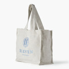 Cream linen tote bag with 'Eleven Bibury' embroidered branding on a white background